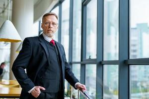 Senior businessman wears modern suir and white shirt. Big window with city view . Photo from the side.