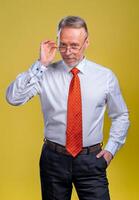 Portrait of a senior man in glasses. Man looking at camera. Business man in studio, yellow backgroung. Man touches glasses. photo