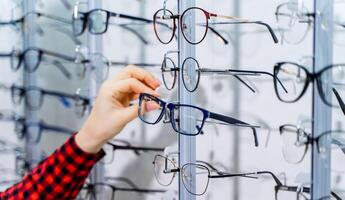 Woman's hand chooses glasses. Presenting spectacles. Row of glasses at an opticians. Eyeglasses shop. Stand with glasses in the store of optics. photo
