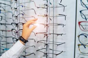 Row of glasses at an opticians. Eyeglasses shop. Stand with glasses in the store of optics. Woman's hand chooses spectacles. Eyesight correction. photo