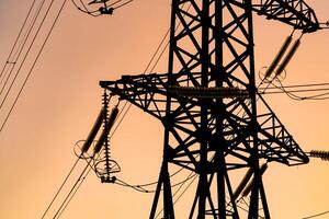 Energy transmission towers or electricity pylons with golden sky and clouds. Selective focus. Cropped photo from below.