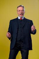 shot of happy senior bearded businessman smiling while dancing and listening to music against yellow background photo