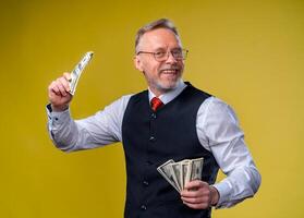 Old smiling grey-haired man in eyeglasses holding fan of dollars in hand. Happy smile on a face. Much money bills. Human emotions and facial expressions. photo
