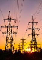 High voltage electric towers at golden sunset. Silhouettes of a number of electricity pylons and trees. Power towers at the background of bright setting sun. photo