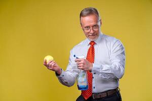 An old man with a beard holds out a yellow apple. Isolated on yellow background. photo