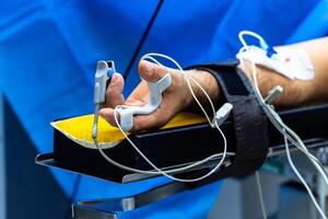 Hand of a patient lying on the operating table. Pulse oximeter sensor on the finger. The patient is sleeping under general anesthesia. photo