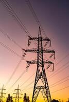 Last rays of the setting sun against the gigantic towers of transmission power lines. Dark thin smoke over the electrical equipment towers at the backdrop of pink and yellow sky. photo