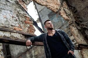 Brutal man posing with mindful expression. Sexy male on abandoned building background. Stock photo