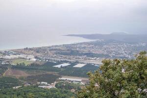 panorámico paisaje urbano y mar ver desde el montaña cubierto con arboles en contra el cielo. Kemer, Turquía foto