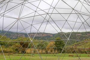 A beautiful scene of multiple geodesic dome tents set up in a tranquil clearing surrounded by vibrant green hills and tall trees. photo