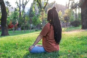 hermosa europeo mujer con largo africano trenzas y étnico decoraciones fuera de en un parque. foto