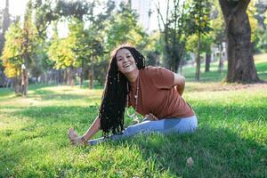 Smiling woman is sitting on a grass and doing yoga exercise. Healthy lifestyle outdoors. photo