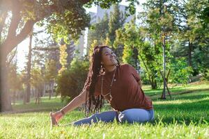 Beautiful young woman with long African braids is doing yoga outside in a park. Concept of healthy lifestyle. photo