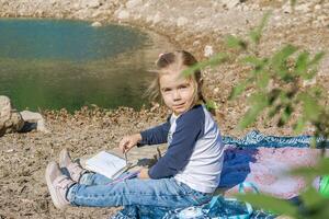 Young girl enjoying a peaceful day by the serene lake, immersed in her art and creativity photo