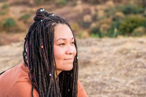 cerca arriba retrato de hermosa europeo mujer con largo africano trenzas en un antecedentes de naturaleza. foto