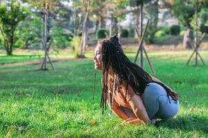 Young woman is sitting on a grass and doing yoga exercise. Healthy lifestyle outdoors. photo