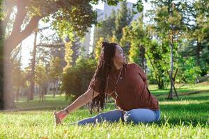 Beautiful young woman with long African braids is doing yoga outside in a park. Concept of healthy lifestyle. photo