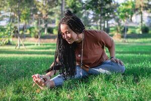 Beautiful young woman with long African braids is doing yoga outside in a park. Concept of healthy lifestyle. photo