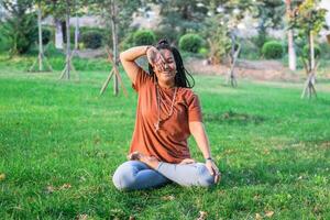 Young woman is sitting in the lotus position and doing breathing exercises in a park. photo