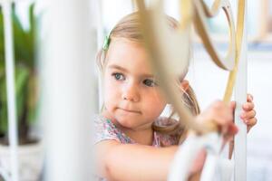 Little girl with blonde hair and blue eyes looks out from behind a white fence. photo