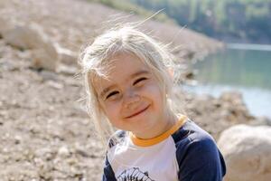 A Joyful Scene Cheerful Girl Relaxing by the Lake on a Sunny Day with a Rocky Backdrop photo