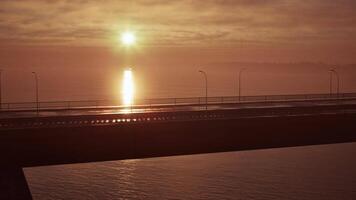 Sol configuração sobre oceano com ponte dentro primeiro plano video