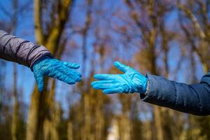 hombre y hembra manos en médico guantes tramo a cada otro. parque con alto arboles borroso antecedentes. selectivo enfocar. coronovirus epidemia. covid-19 y coronavirus identificación. pandemia foto