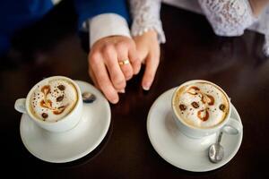 Image of two people's hands with wedding rings. Coffee or hot chocolate cups on wooden table in a cafe. photo
