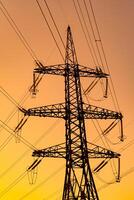 Below angle view of electricity pylons bearing electricity to a city or town. Orange sunset background. photo