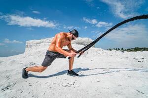 Fitness athlete in a cap and sunglasses training with ropes outdoor. photo