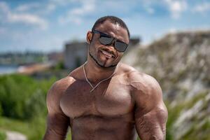 Portrait of handsome muscular in sunglasses. Young guy athletic body. photo