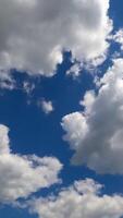Cloudscape building in the blue sky. Soft puffy clouds flying quickly. Low angle perspective. Timelapse. Vertical video