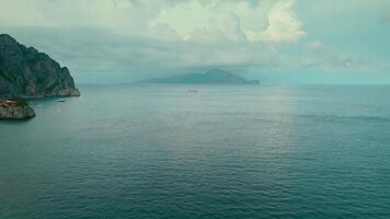 neblig Seelandschaft mit Segeln Schiff in der Nähe von Capri unter bedeckt Himmel. diese maritim Szene erfasst ein hoch Schiff gleiten Vergangenheit das Insel prominent Klippen im gedämpft Licht. video