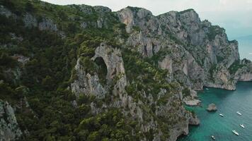 Cliffside arches of Capri overlook sea waters and anchored yachts. The natural arch formations and rugged coastline with maritime vessels on tranquil bay below. video