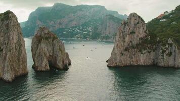 Picturesque sea arches carved into towering cliffs by the ocean's might. The natural bridges create a gateway for boats. Faraglioni sea stacks in Capri, Italy. video