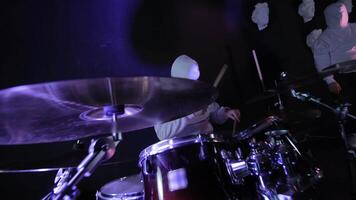 Hooded Drummer Performing on Stage, Mysterious figure in white hoodie playing drums, surrounded by red lights. video