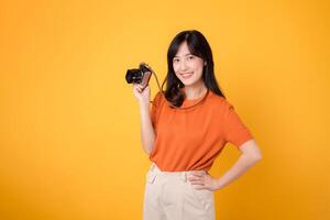 Happy asian lady with a camera isolated on yellow background, eager for an unforgettable holiday journey. photo