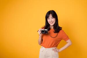 Smiling lady traveler holding a camera isolated on yellow background, illustrating the joy of a holiday journey. photo