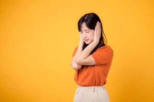 Tired asian woman 30s shouting in reaction to loud noise, covering her ear. Expression of stress and frustration isolated on yellow background. photo