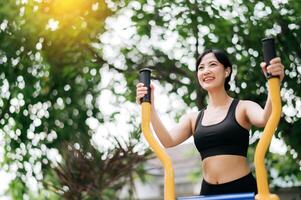 Young asian athletic sportswoman 30s wearing sportswear listening relaxing music while working out exercise equipment outdoor in park. Healthy lifestyle concept photo