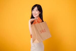 Trendy asian woman 30s in orange shirt celebrating a shopping spree with discounted purchases. Happy shopping concept. photo