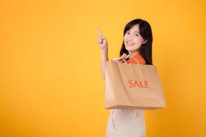 elegante mujer señalando a gratis Copiar espacio mientras participación pantalones durante un rebaja aislado en amarillo fondo, disfrutando un compras juerga con excitación. moda vanguardista opciones foto