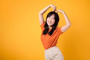 Radiate positivity and connection as an Asian woman in her 30s dons an orange shirt, forming a heart shape with her arms, symbolizing love and unity. photo