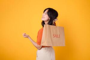 Experience the thrill of finding bargains in a trendy mall setting. Smiling asian woman 30s showcases her shopping haul, reflecting the joy of smart purchases. photo