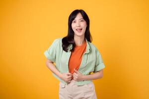 happiness and well-being with cheerful young Asian woman 30s wearing an orange shirt. Her happy mind wellness gesture on a yellow background captures a profound happiness portrait of contentment. photo