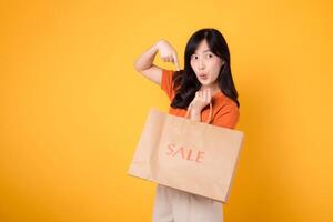 Experience the thrill of finding bargains in a trendy mall setting. Smiling asian woman in her 30s showcases her shopping haul, reflecting the joy of smart purchases. photo