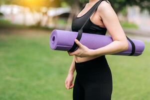 Health-conscious Asian woman stands with a rubber mat in the park, gearing up for sunset exercises. Wellness, activity, and natural beauty. photo