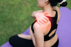 Woman jogger. young 30s asian female wearing black sportswear holding her shoulder pain after exercise in public park. Pain in activity concept. photo
