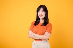 Embrace confidence with a young Asian woman in her 30s, donning an orange shirt, displaying crossed arm sign gesture on yellow background. photo