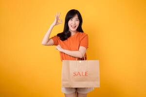 joven asiático mujer 30s con bueno firmar mano gesto aislado en amarillo antecedentes. abrazo compras felicidad con alegre sonrisas y descuentos de moda mujer participación un bolso en un alegre concepto. foto